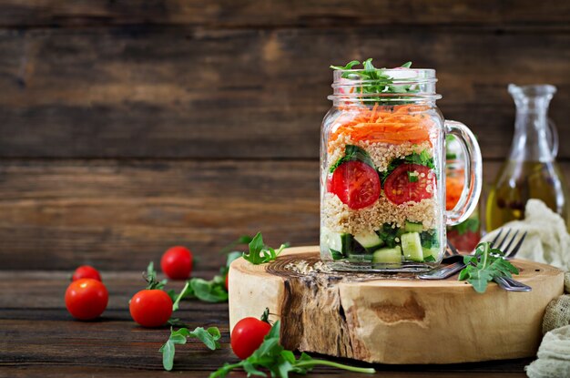 Ensaladas con quinua, rúcula, rábano, tomate y pepino en frascos de vidrio sobre mesa de madera. Comida sana, dieta, desintoxicación y concepto vegetariano