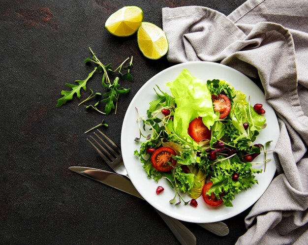 Ensaladera mixta verde fresca con tomates y microgreens sobre superficie de hormigón negro