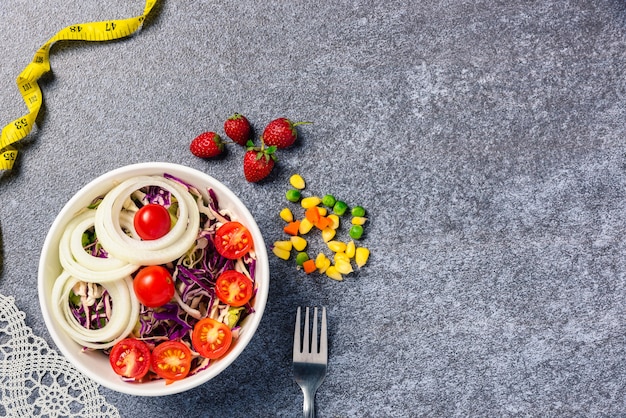 Ensaladera saludable con tomates frescos vegetales mixtos en un plato y cinta métrica