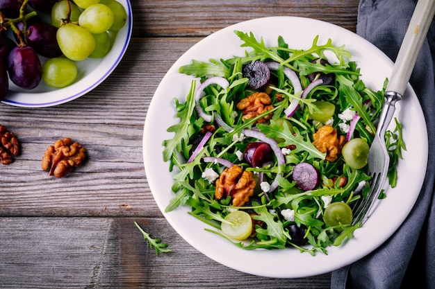 Ensaladera verde con rúcula, nueces, queso feta, cebolla roja y uvas sobre fondo de madera