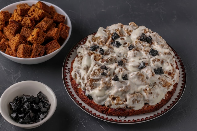 Ensamblar el pastel Pancho a partir de rebanadas de bizcocho, crema agria y ciruelas pasas, el proceso culinario en una superficie oscura