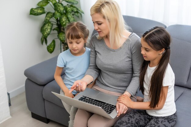 Enseñar en casa a dos hijas pequeñas que aprenden Internet en línea hacen la tarea usando la computadora con la ayuda de la madre, enseñan y alientan. Niña y hermana pequeña felices de estudiar educación en casa juntas.