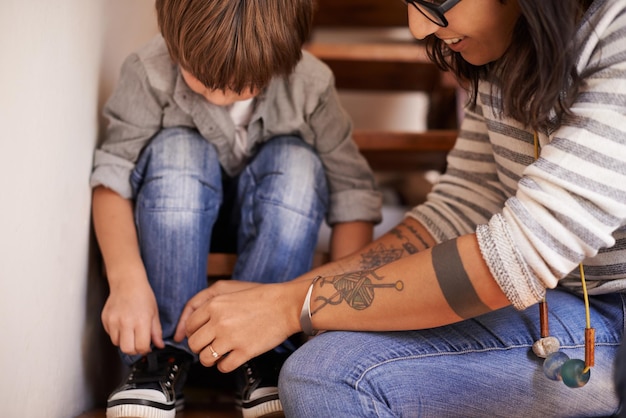 Ensinando-o a amarrar os sapatos Uma jovem mãe ajudando o filho a amarrar os sapatos