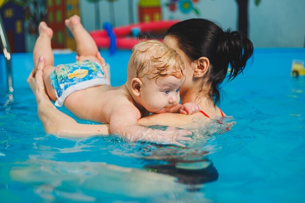 Ensinando um menino recém-nascido a nadar na piscina com um treinador Cursos de natação para bebês A criança nada na piscina