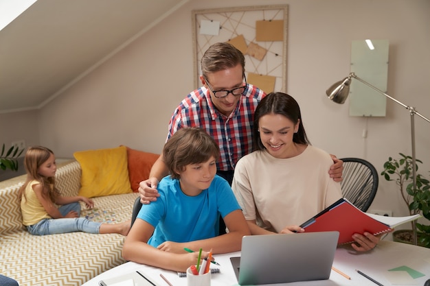 Ensinar em casa jovens pais positivos ajudando seu filho com os deveres de casa enquanto sua irmã está sentada