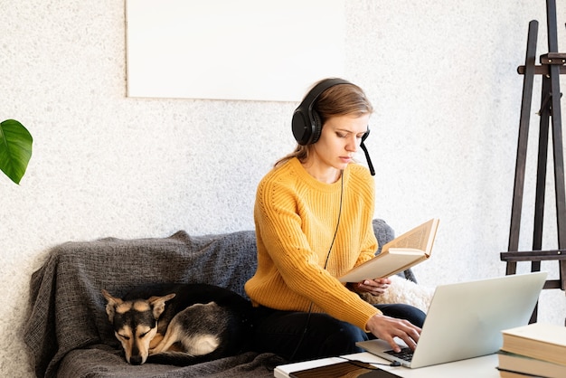 Ensino à distância. e-learning. jovem mulher sorridente com suéter amarelo e fones de ouvido pretos, estudando on-line usando um laptop, sentada no sofá em casa