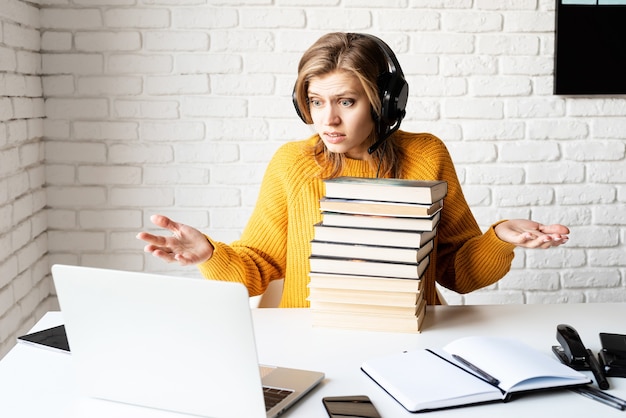 Ensino à distância. e-learning. mulher jovem com fones de ouvido pretos estudando on-line e segurando uma pilha de livros