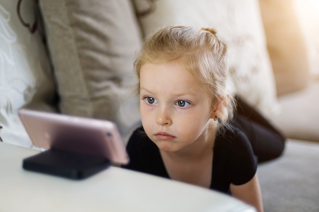 Ensino a distância, educação on-line para crianças. menina estudando em casa na frente do telefone. criança assistindo desenhos animados on-line, crianças dependência de computador, conceito de controle parental.