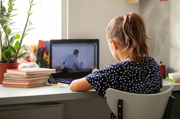 Ensino a distância online, uma colegial com um computador, se comunica com um professor via videoconferência.