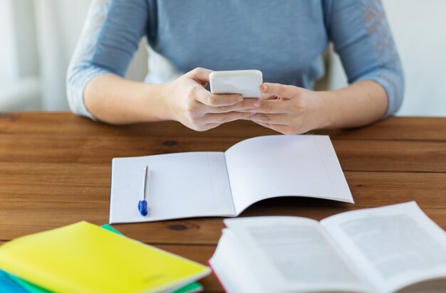 ensino médio, educação, pessoas e conceito de aprendizagem - close-up de jovem estudante ou mulher com smartphone, livro e notebook em casa