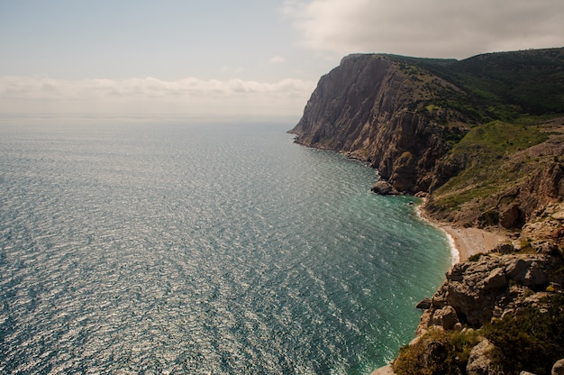 Foto ensolarada baía rochosa, banhada pelo mar azul