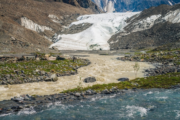 Ensolarada paisagem alpina com confluência de dois vários rios de montanha.