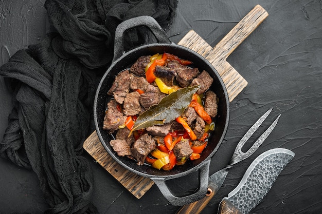 Ensopado de carne bangin servido, em frigideira de ferro fundido, sobre fundo de pedra preta, vista de cima plana, com espaço de cópia para o texto