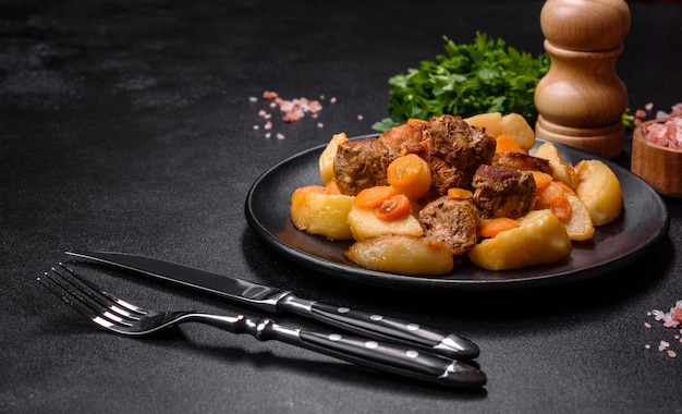 Ensopado de carne e legumes em um prato preto com batatas assadas