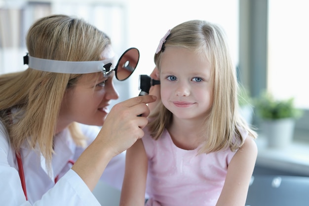 Ent médico mira las orejas de las niñas con primer otoscopio