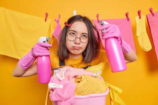 Entediada, cansada e exausta zeladora asiática segurando dois frascos de detergente de limpeza, ocupada fazendo luandry e limpando a casa