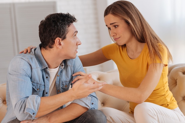 Entendiendo a la mujer. Mujer joven bastante alegre que apoya a su marido mientras está sentado y escucha su historia