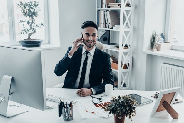 Entendimento mútuo. Jovem bonito em trajes formais falando ao telefone e sorrindo