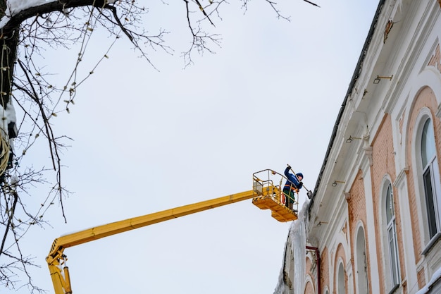 Entfernen von Eiszapfen und Schnee vom Dach des Hauses mit einem Aufzug Vermeidung von unsicheren Situationen für Fußgänger auf den Straßen der Stadt