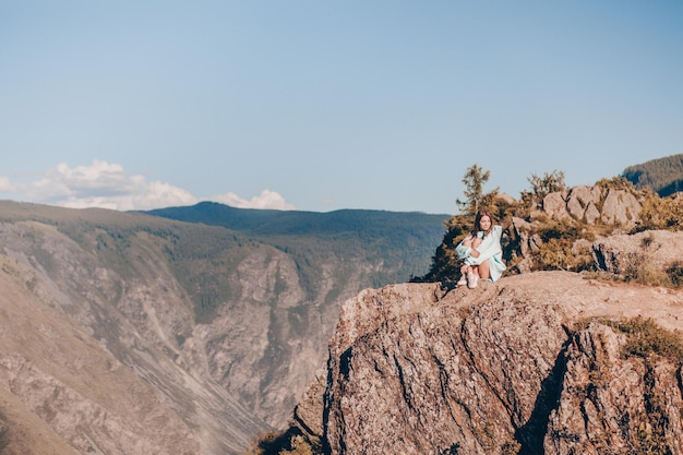 Entferntes Bild vom Kopter. Ein Mädchen in einem blauen Hoodie sitzt mit angezogenen Beinen auf einer Klippe und schaut weg. Herrliche Aussicht auf die Berge.
