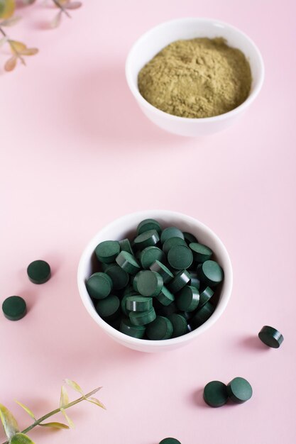 Entgiftungs- und Antioxidans-Matcha-Pulver und Spirulina-Pillen in Schalen auf einer rosafarbenen vertikalen Ansicht