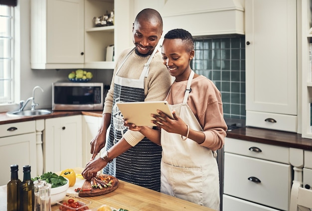 Entonces, ¿qué dice la receta? Captura recortada de una joven pareja cariñosa usando una tableta mientras prepara la cena en su cocina.