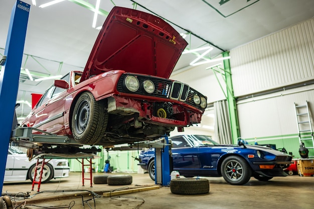 En un entorno de taller de automóviles completamente equipado hay dos coches clásicos que se están cuidadosamente