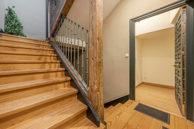 Entrada a una casa con una antigua puerta con paneles pintados de verde mate y escaleras de madera de pino con columnas de madera