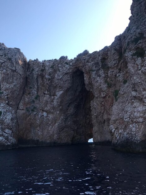 Entrada do buraco de pedra ou abertura na parede da caverna rochosa olhando para o céu e o mar