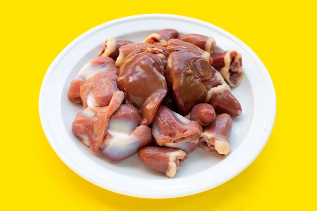 Entrañas de pollo mixtas en plato blanco sobre fondo amarillo.