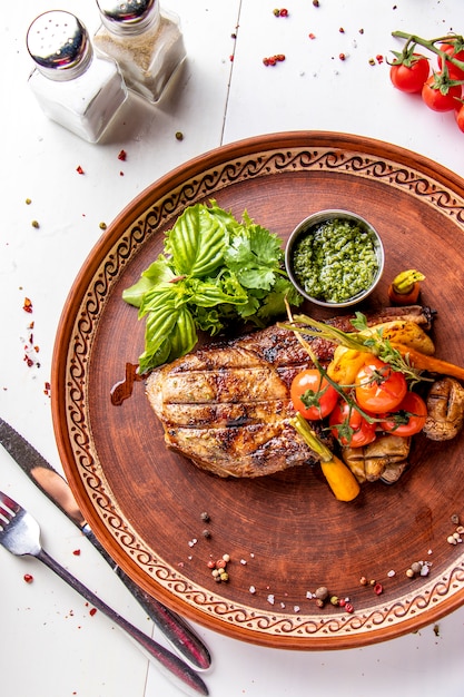 Entrecot de cerdo servido con verduras a la parrilla, champiñones y salsa de pesto, plato de restaurante, vista superior, orientación vertical