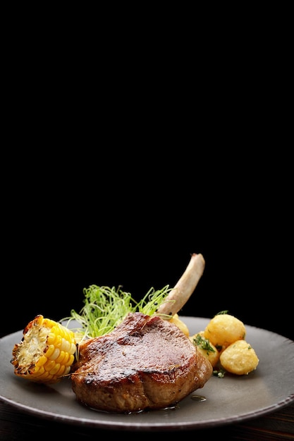 Foto entrecot de ternera con patatas y maíz en un plato sobre un fondo de madera vertical