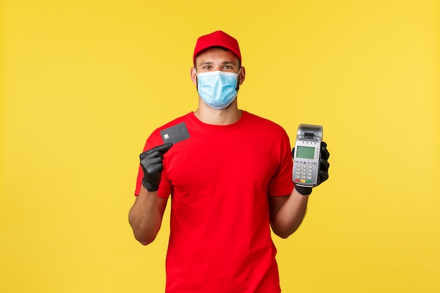 Entrega de alimentos, seguimiento de pedidos, covid-19 y concepto de auto cuarentena. Mensajero con uniforme rojo, máscara médica y guantes, mostrando terminal POS y tarjeta de crédito, pago sin contacto durante el coronavirus