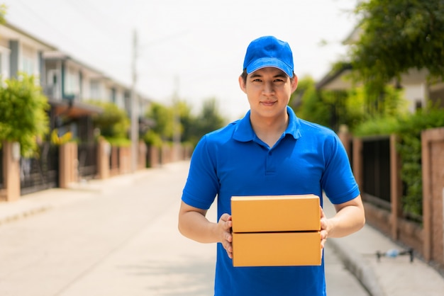 Entrega asiática joven en uniforme azul sosteniendo una caja