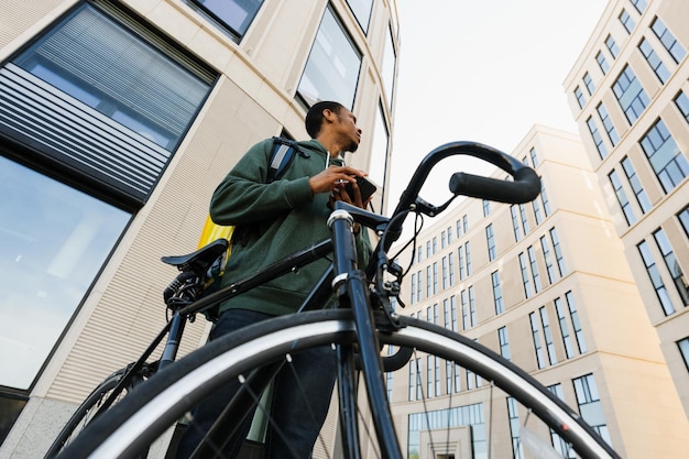 Entrega en la ciudad en bicicleta Mensajero afroamericano con una mochila amarilla afuera