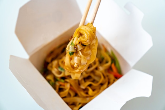 Entrega de comida asiática preparada. fideos con verduras y mariscos en una caja blanca y palitos de sushi. Deliciosa cena. pedir comida por teléfono o en línea.