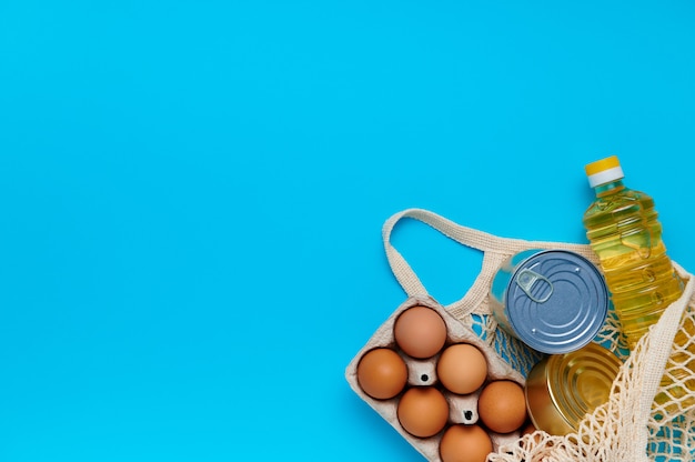 Entrega de comida, donación. Conjunto de huevos, comida enlatada, aceite dentro de una bolsa de hilo en azul