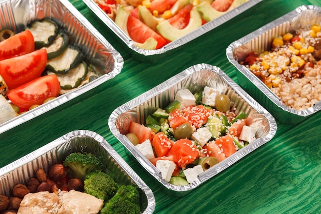 Entrega de comida de restaurante saludable. Comida para llevar en loncheras de aluminio con espacio para copiar en madera verde. Ensaladas, carnes y frutas.