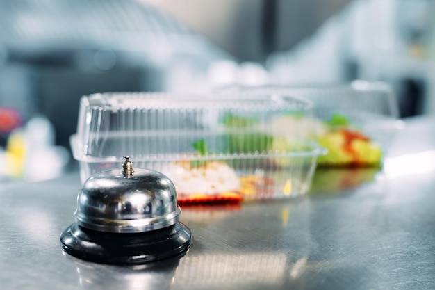 Entrega de alimentos. mesa de distribuição em um restaurante com campainha de metal. alimentos em recipientes de plástico. panna cotta e salada de legumes em recipientes descartáveis de plástico.