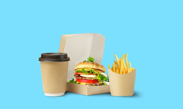 Entrega de almoço de fast food. Saboroso hambúrguer, batatas fritas e café em embalagem de papelão sobre fundo azul.