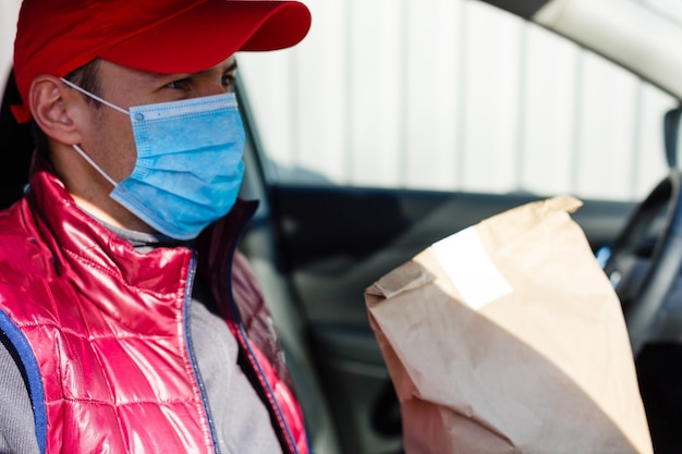 entrega de carro. homem com máscara protetora e luvas médicas, segurando uma caixa de papel. Serviço de entrega em quarentena, surto de doença, condições de pandemia de coronavírus covid-19.