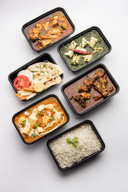 Entrega de comida online com masala indiana de manteiga paneer e palak paneer, caril de carneiro e frango com roti e arroz em recipientes de plástico