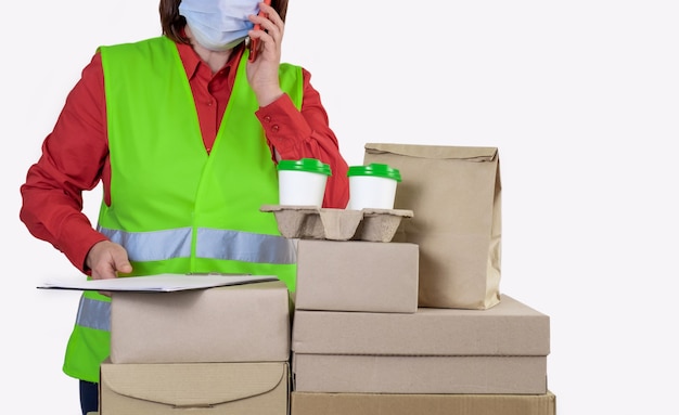 La entrega está en un chaleco verde que sostiene cajas de papel y un recipiente para llevar con dos tazas blancas de café.