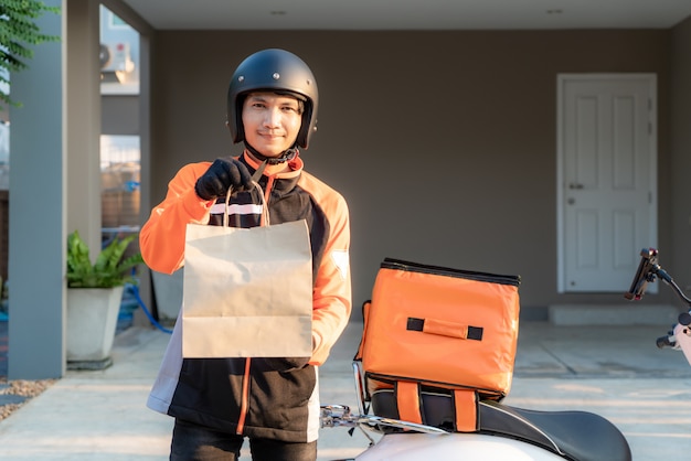 Entrega Hombre asiático vistiendo uniforme naranja y listo para enviar entregando bolsa de comida en frente de los clientes con caja de caja de comida en scooter, entrega de comida rápida y compras en línea concepto.