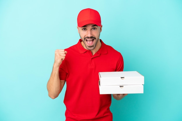 Foto entrega hombre caucásico recogiendo cajas de pizza aisladas sobre fondo azul celebrando una victoria en posición de ganador