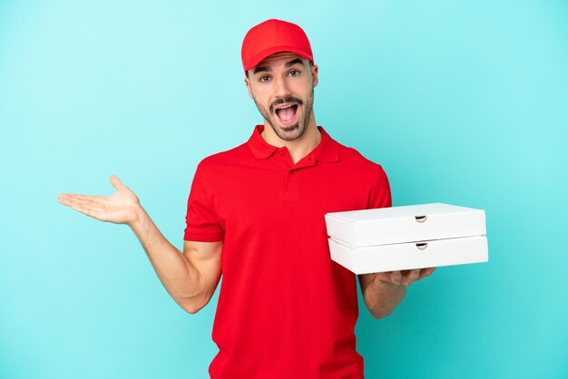 Entrega hombre caucásico recogiendo cajas de pizza aisladas sobre fondo azul con expresión facial sorprendida