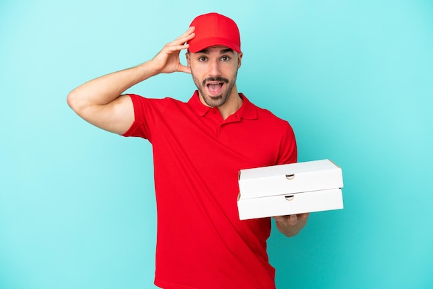 Entrega hombre caucásico recogiendo cajas de pizza aislado sobre fondo azul con expresión de sorpresa