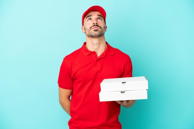 Entrega hombre caucásico recogiendo cajas de pizza aislado sobre fondo azul y mirando hacia arriba