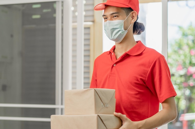 Entrega jovem asiático carteiro masculino segurando caixa de papelão ou correio em uniforme vermelho enviar ao cliente cliente recebido do mensageiro em casa Serviço de compras on-line