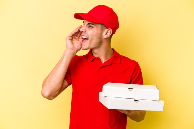 Entrega joven hombre caucásico sosteniendo pizzas aisladas sobre fondo amarillo gritando y sosteniendo la palma cerca de la boca abierta